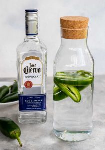 Making silver jalapeno tequila at home in a glass jar, jose cuervo silver tequila and a bowl of jalapenos