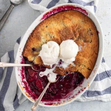 an oval dish with berry cobbler and two scoops of ice cream. two spoons sticking out of the side