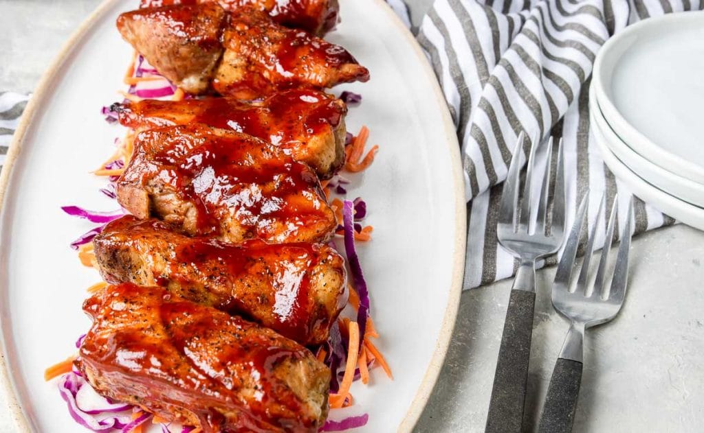 Instant Pot Country Style Ribs coated with bbq sauce on a white plate over coleslaw