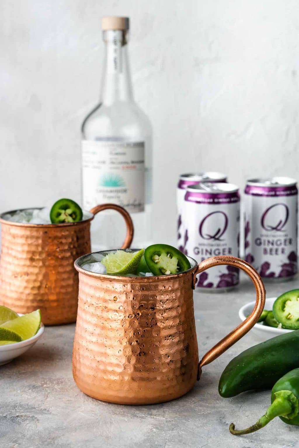 Tequila Moscow Mule in a copper mug with a bottle of tequila, jalapenos and ginger beer