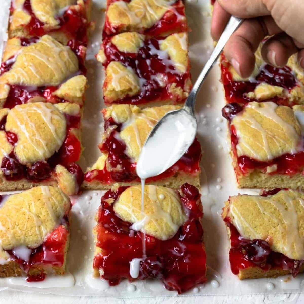 cherry pie bars cut into squares with glaze being drizzled on top