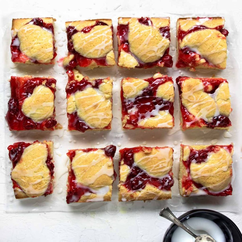 Homemade cherry Pie Bars cut into squares and laid on parchment paper, drizzled with frosting glaze