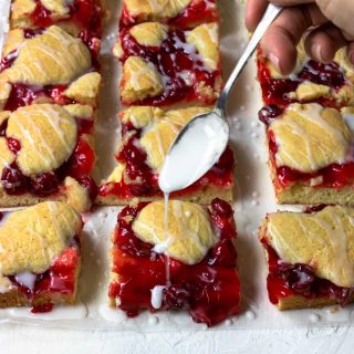Easy cherry pie bars cut into squares and being drizzled with powdered sugar glaze