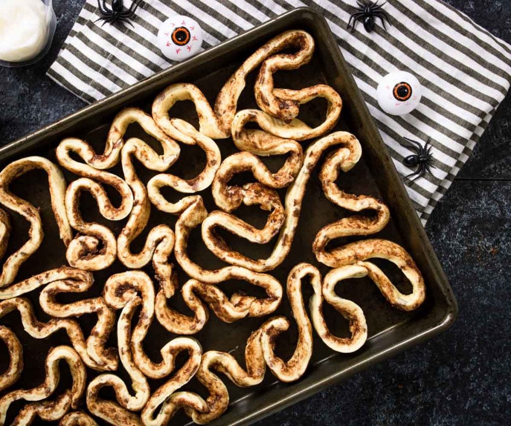 Baking sheet full of uncooked cinnamon rolls that are unraveled - looks like intestines
