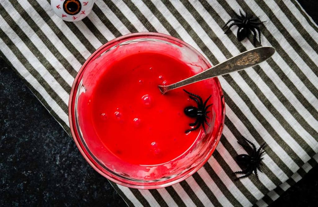 Red frosting in a bowl with a plastic spider on the side