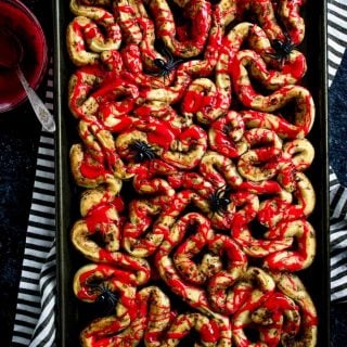 Halloween Breakfast Bloody Guts Cinnamon Rolls on a baking sheet drizzled with red frosting and plastic spiders