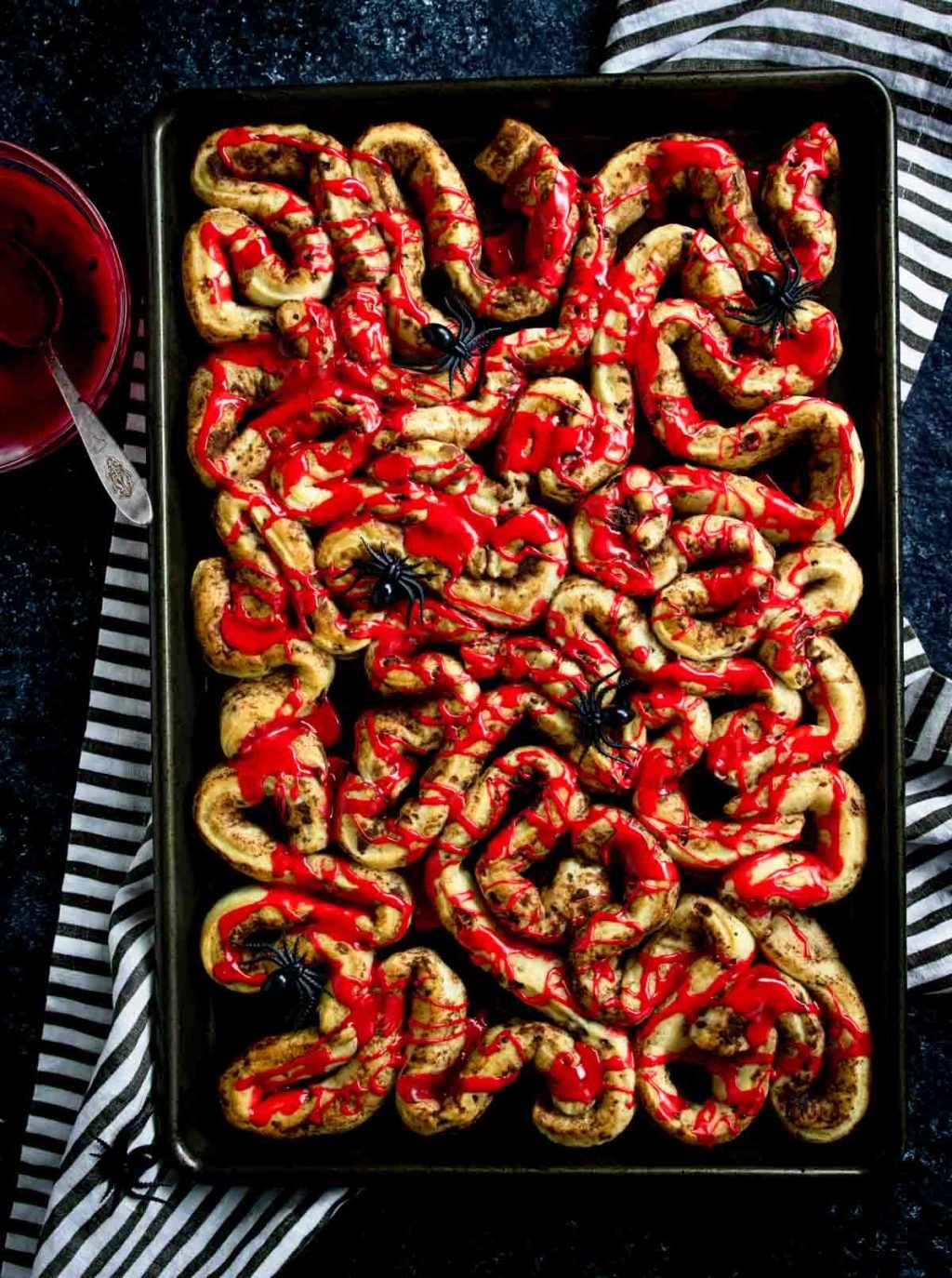 Halloween Breakfast Bloody Guts Cinnamon Rolls on a baking sheet drizzled with red frosting and plastic spiders