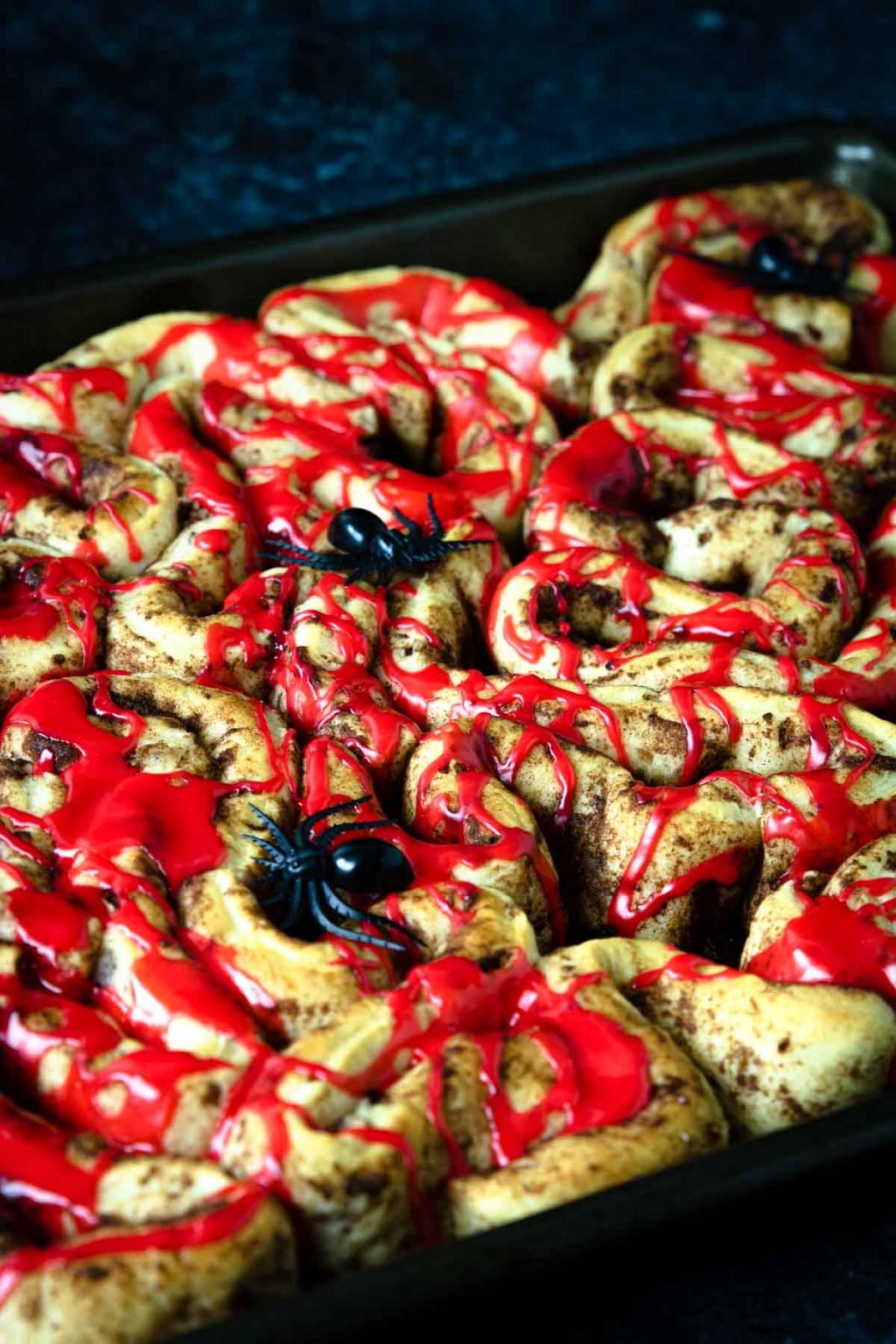 Bloody Guts Cinnamon Rolls covered in red frosting and plastic spiders, perfect halloween breakfast