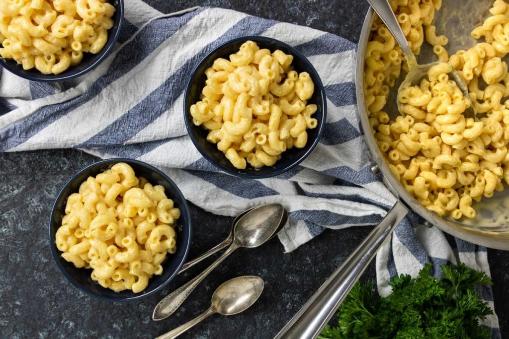 three bowls of homemade macaroni and cheese and a skillet to the side