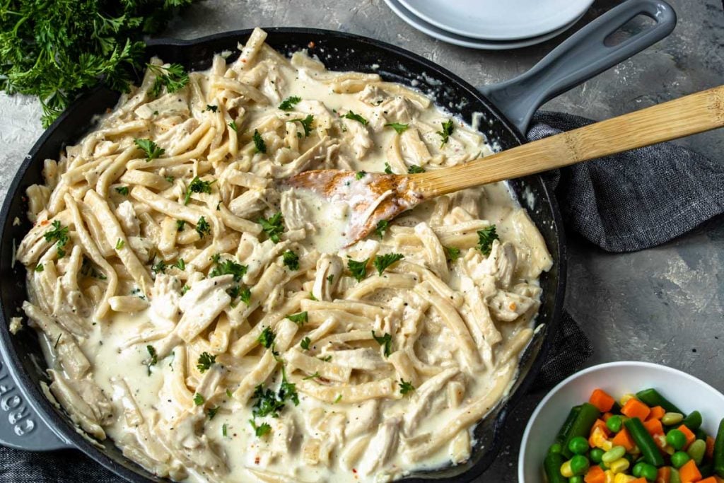 Creamy Chicken and Noodle recipe made in a large grey skillet, mixed veggies to the side