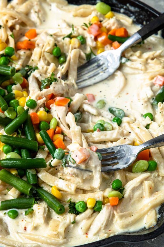 Creamy Chicken and Noodles in a skillet with mixed veggies added on top