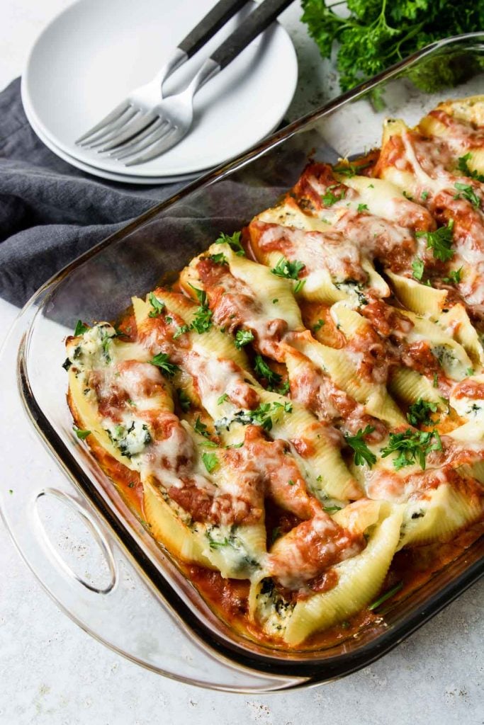 Vegetarian Stuffed Shells in a glass baking dish with two plates and two forks to the side