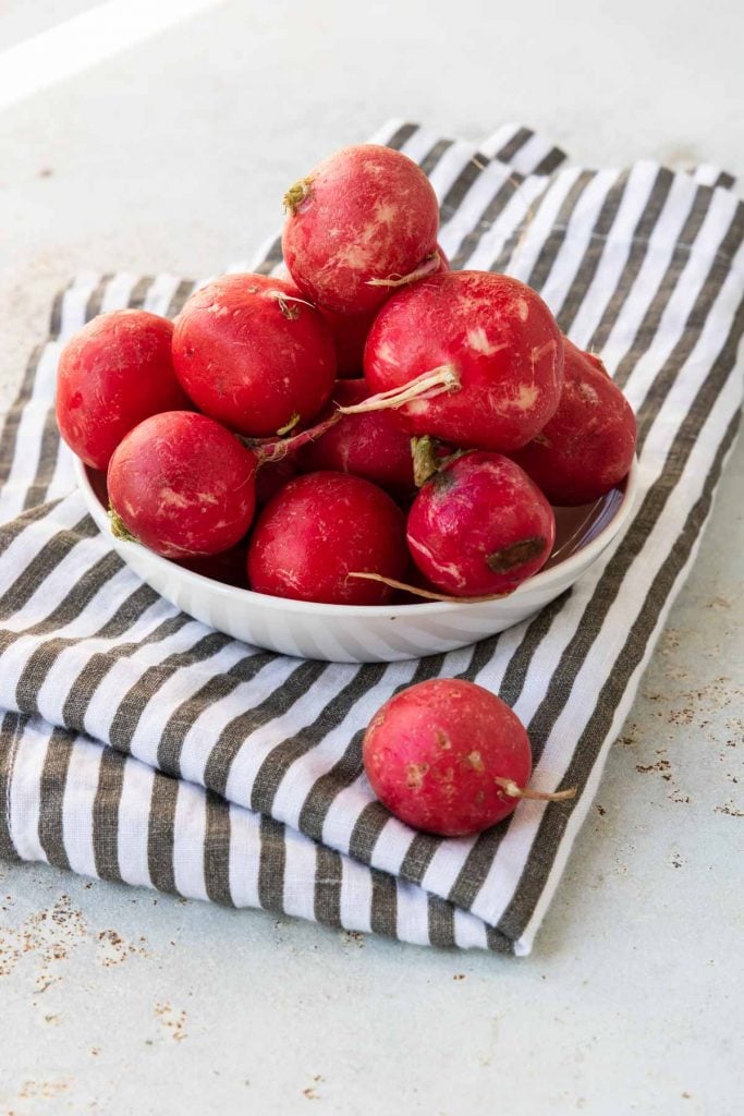 fresh radishes in a white bowl on a black and white napkin