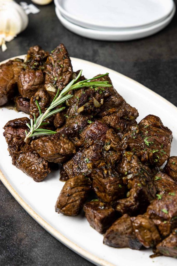 Pan seared steak bites in a garlic butter sauce on a white plate topped with rosemary