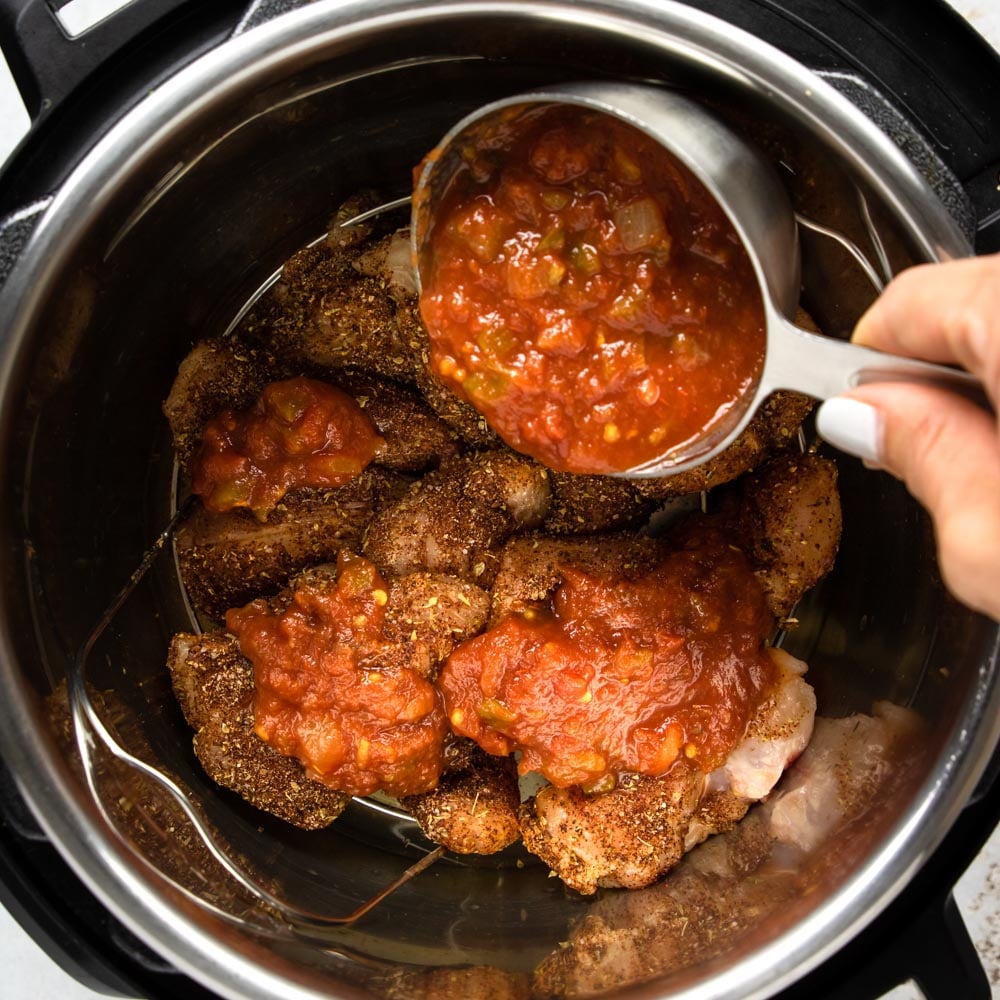 pouring salsa over the seasoned chicken in the instant pot