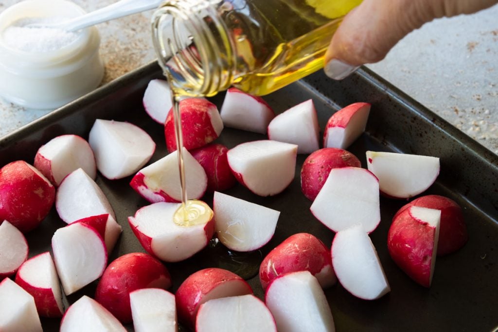 Olive oil being poured on cut radishes