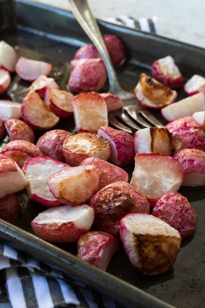 radishes roasted on a baking sheet with a fork