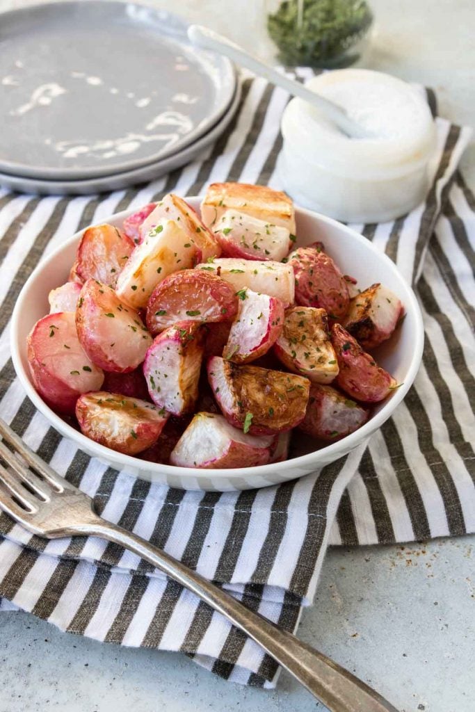 Oven roasted radishes in a white bowl on a black and white napkin