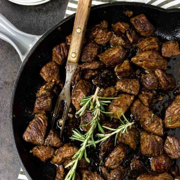 Garlic Butter Steak Bites in a skillet with a meat fork and topped with rosemary