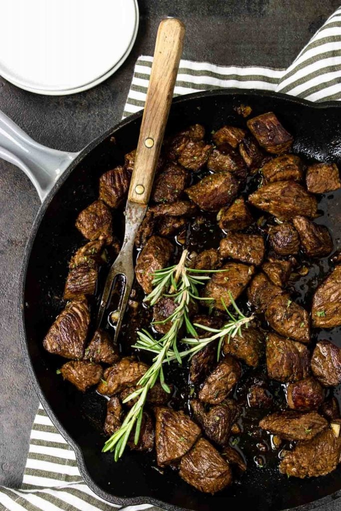 Garlic Butter Steak Bites in a skillet with a meat fork and topped with rosemary