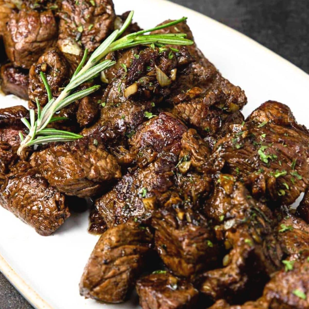 garlic butter steak bites on a platter with a sprig on rosemary