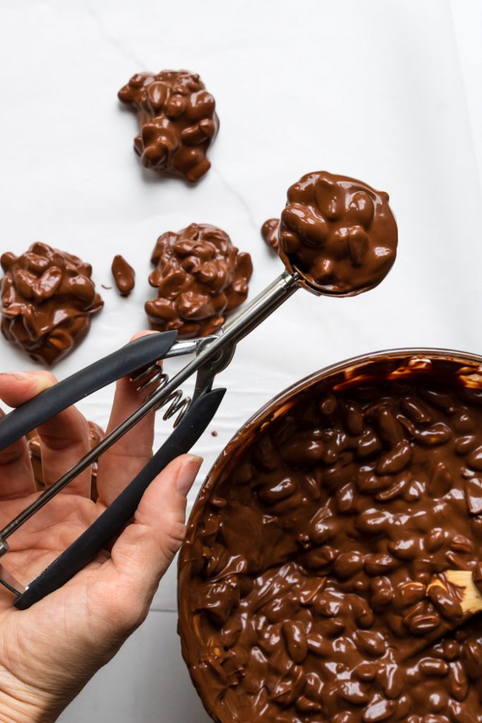 Using a scoop to drop chocolate peanut clusters on wax paper