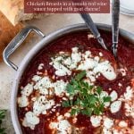 A large skillet with chicken in a tomato sauce topped with goat cheese- pinterest text over top