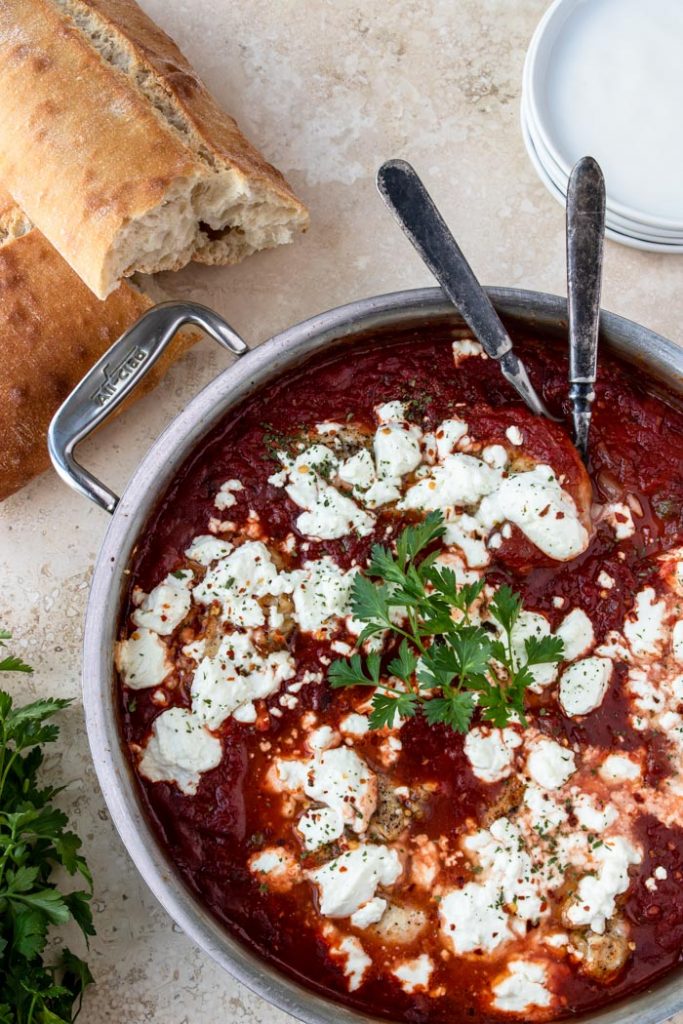 Chicken in a red sauce topped with goat cheese, crusty bread to the side.