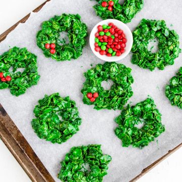 Green Christmas Wreath cookies on a baking sheet with a bowl of red M&M's