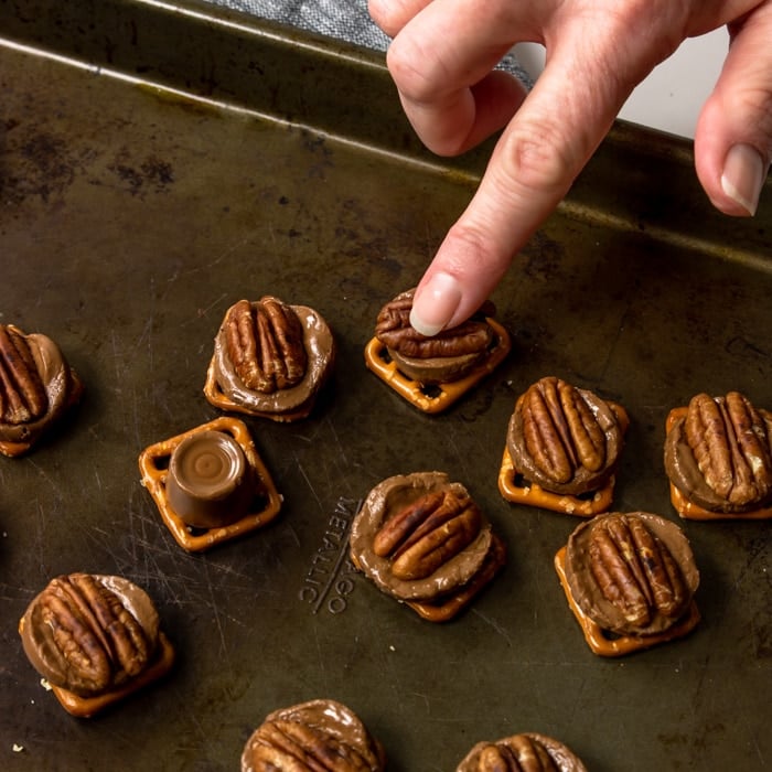 Pressing a toasted pecan into the middle of the soft Rolo on top of a preztel