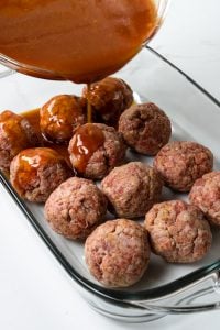 pouring the tomato brown sugar sauce over the ham balls