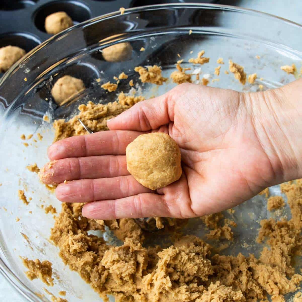 Rolling a ball of peanut butter cookie to be baked in a muffin tin