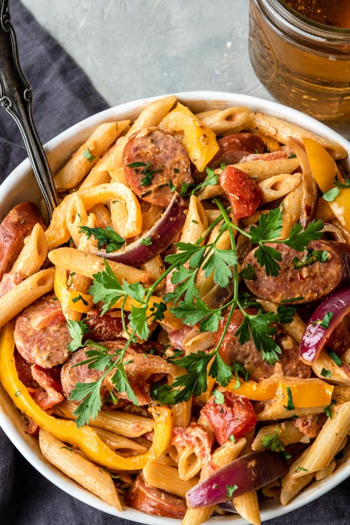penne pasta, smoked sausage, onions and peppers in a cajun cream sauce in a large white bowl garnished with parsley