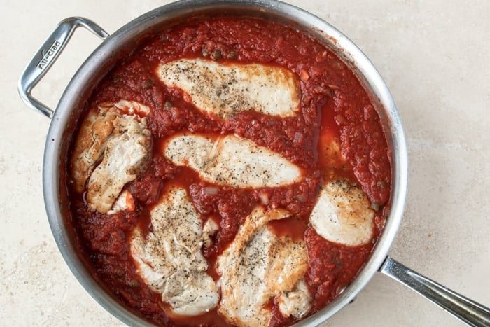 Browned Chicken breasts nestled down in a red wine tomato sauce