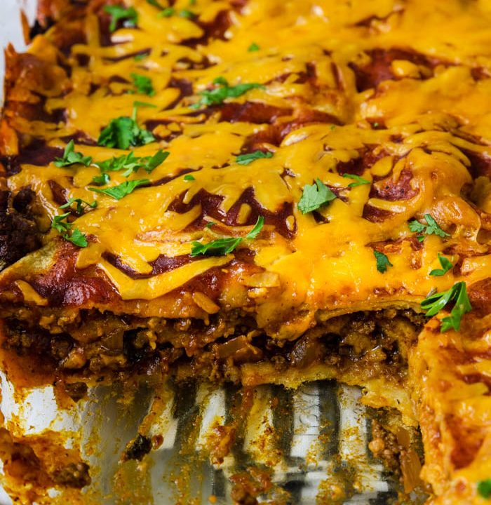 beef enchilada Casserole with a slice cut out so you can see the layers of corn tortillas, beef, cheese and sauce