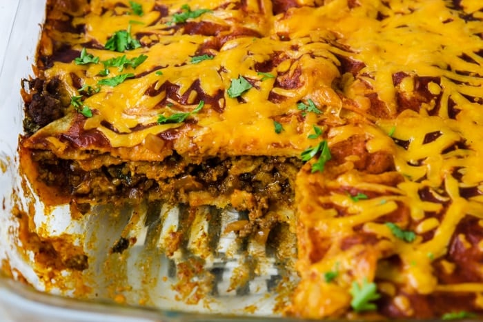 beef enchilada casserole with a piece taken out so you can see the layers of tortillas, beef, cheese, and sauce
