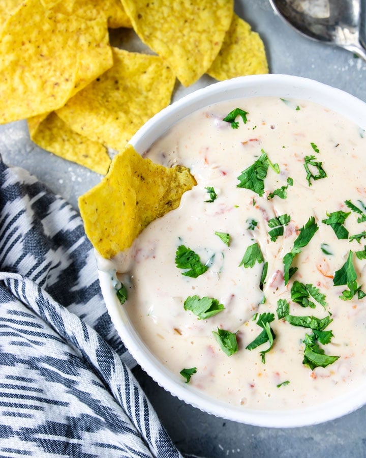 Bowl of IP Queso topped with cilantro and a chip dipped in the side
