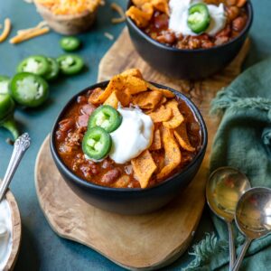 a bowl of chili made in the instant pot with jalapenos, fritos and sour cream on top