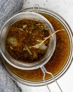 a mesh collander with solids from the instant pot pork roast stained into a glass bowl