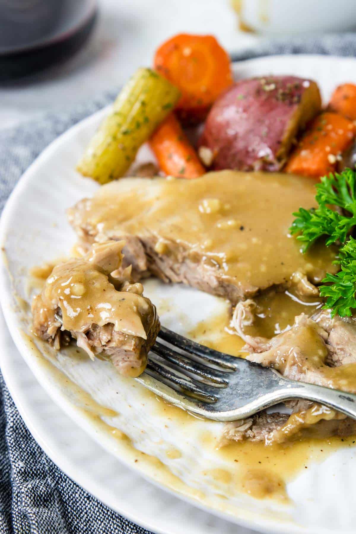 a sliced of pork roast on a fork with gravy and veggies in the back
