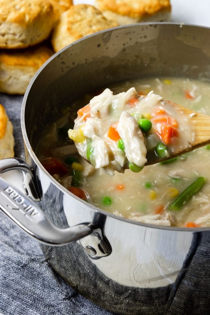A spoon full of chicken and veggie stew with biscuits in the background