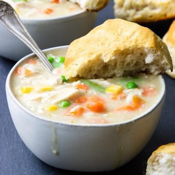 Chicken and biscuits in a white bowl with biscuits in the background