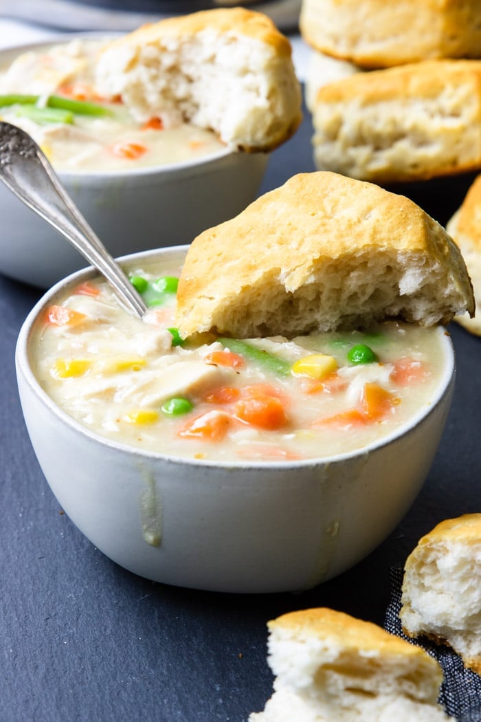 Chicken and biscuits in a white bowl with biscuits in the background