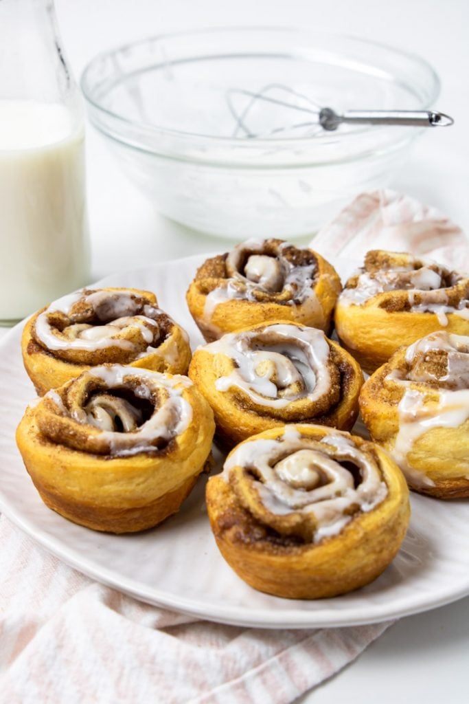 crescent cinnamon rolls on a white plate with frosting in the background
