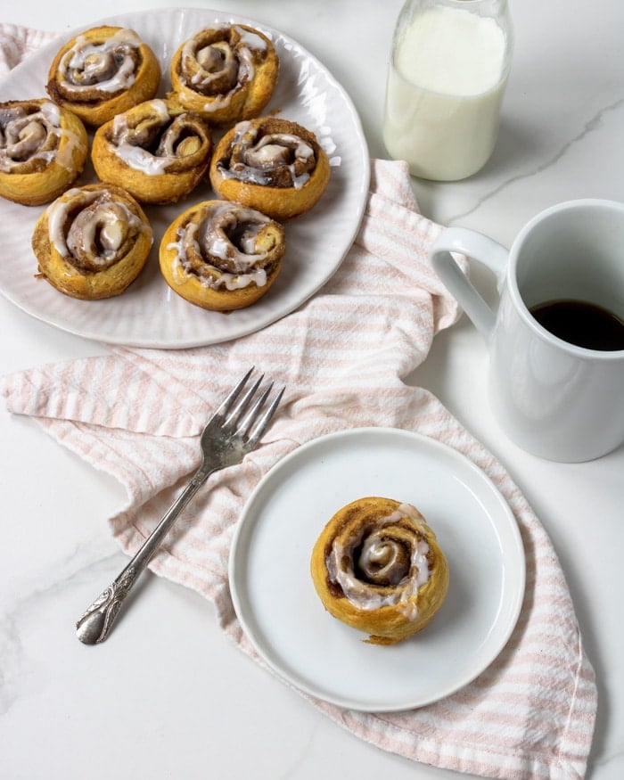 cinnamon roll on a white plate with coffee and a fork