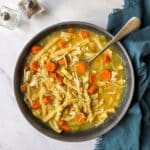 A bowl of Instant Pot Chicken Noodle Soup with a spoon and cracked black pepper on top