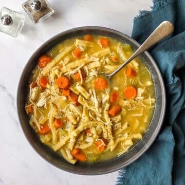 A bowl of Instant Pot Chicken Noodle Soup with a spoon and cracked black pepper on top