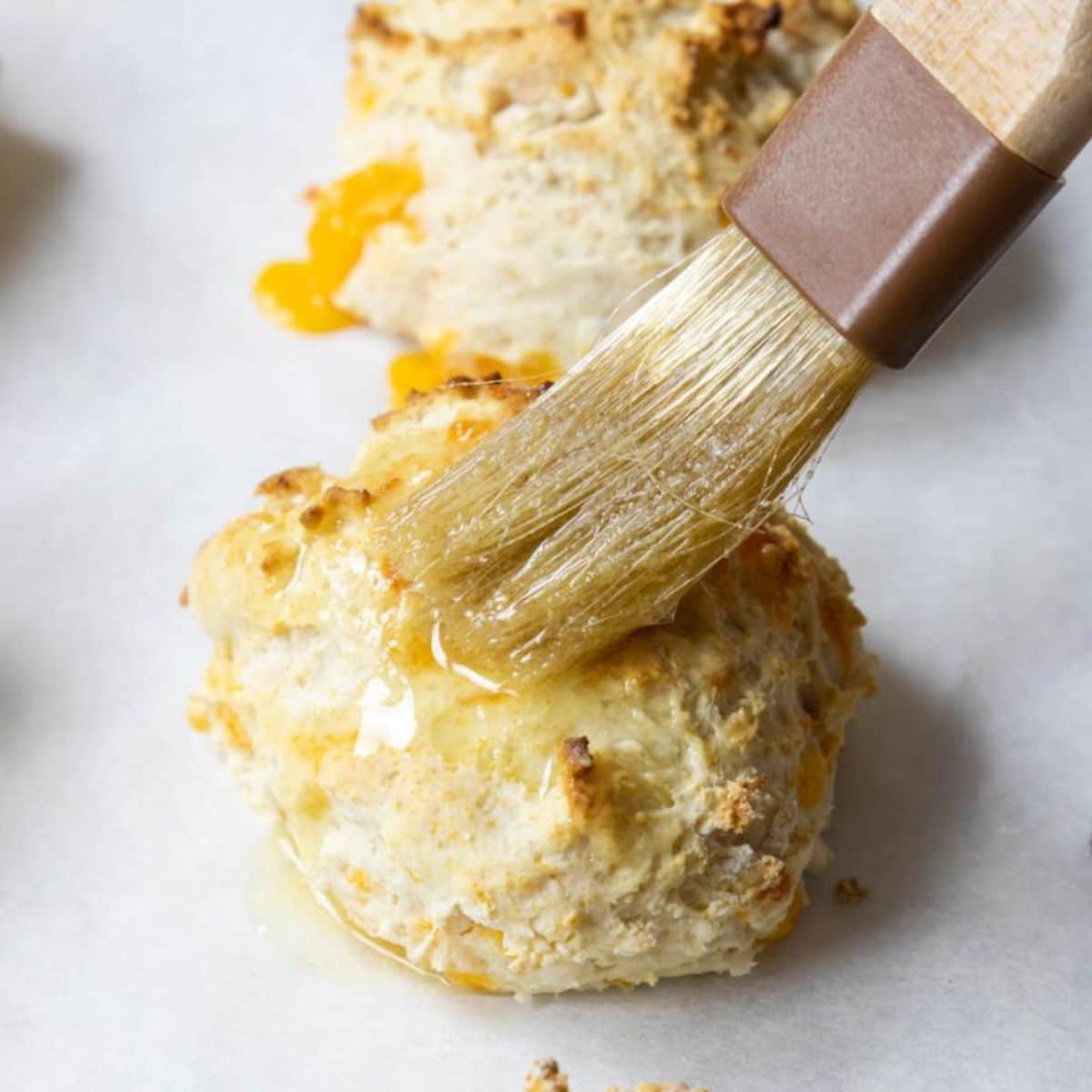 Brushing garlic butter on a cheddar biscuit.