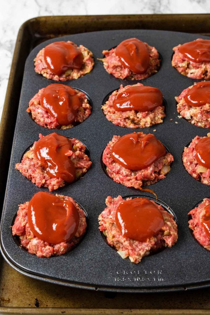 raw meatloaf muffins in a muffin tin topped with ketchup