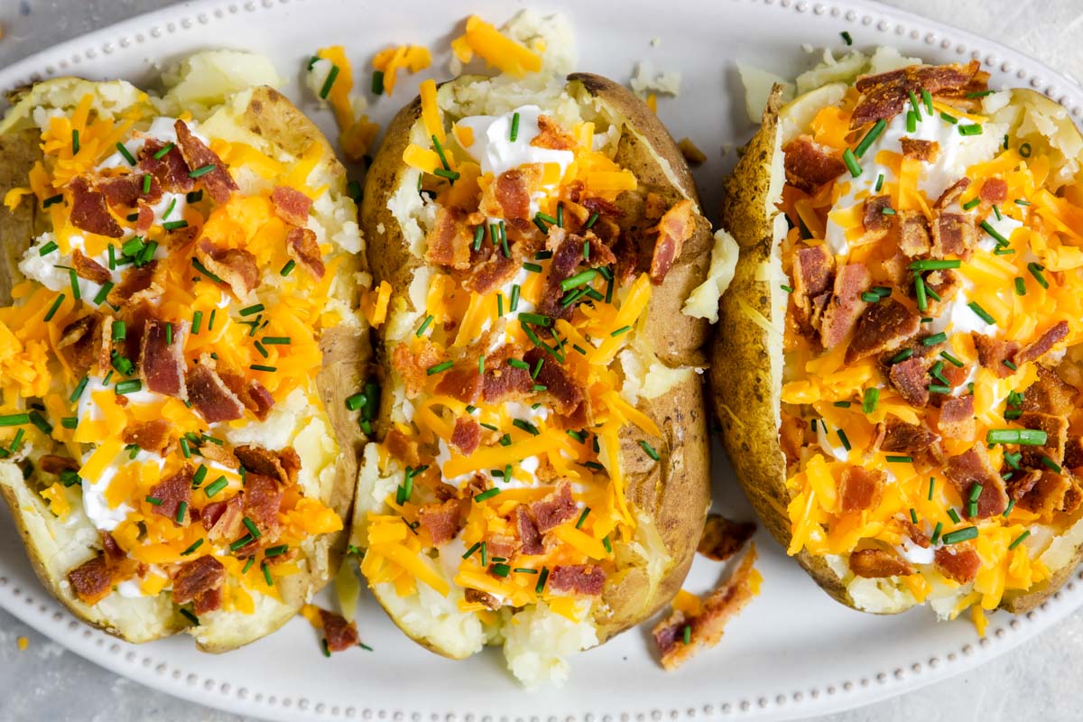 three baked potatoes on a plate stuffed with cheese and bacon